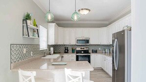 Une cuisine moderne avec des meubles blancs, un plan de travail en granit, un réfrigérateur en acier inoxydable et deux suspensions.