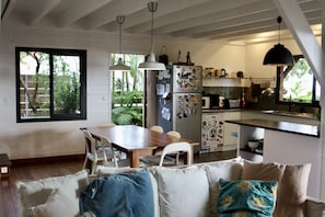 A modern kitchen with a dining area, featuring a wooden table, white chairs, and pendant lighting.