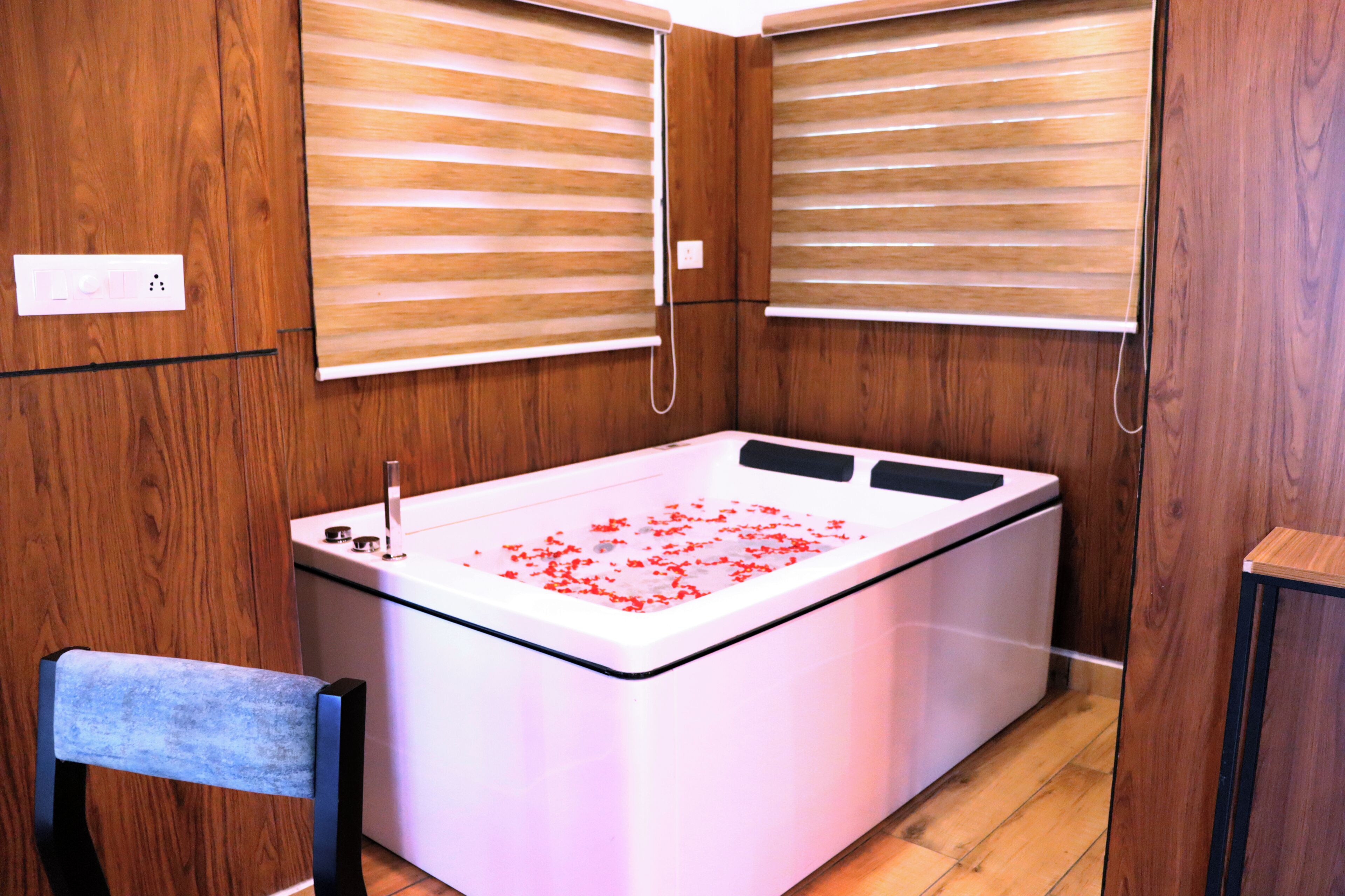 A room with a large bathtub, wooden walls, and a small chair.
