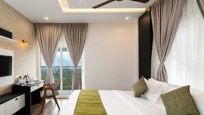 A modern hotel room with a bed, a desk, a TV, and a view of the outdoors. - Ramee Wolkenburg Resort and Spa Munnar (Devikolam)