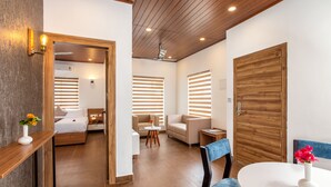 A modern hotel room with a wooden ceiling, a bed, a sofa, a dining table, and a small side table. - Ramee Wolkenburg Resort and Spa Munnar (Devikolam)