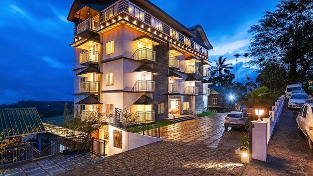 A multi-story hotel with balconies, a paved driveway, and cars parked outside. - Ramee Wolkenburg Resort and Spa Munnar (Devikolam)