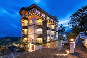 A multi-story hotel with balconies, a paved driveway, and cars parked outside. - Ramee Wolkenburg Resort and Spa Munnar (Devikolam)