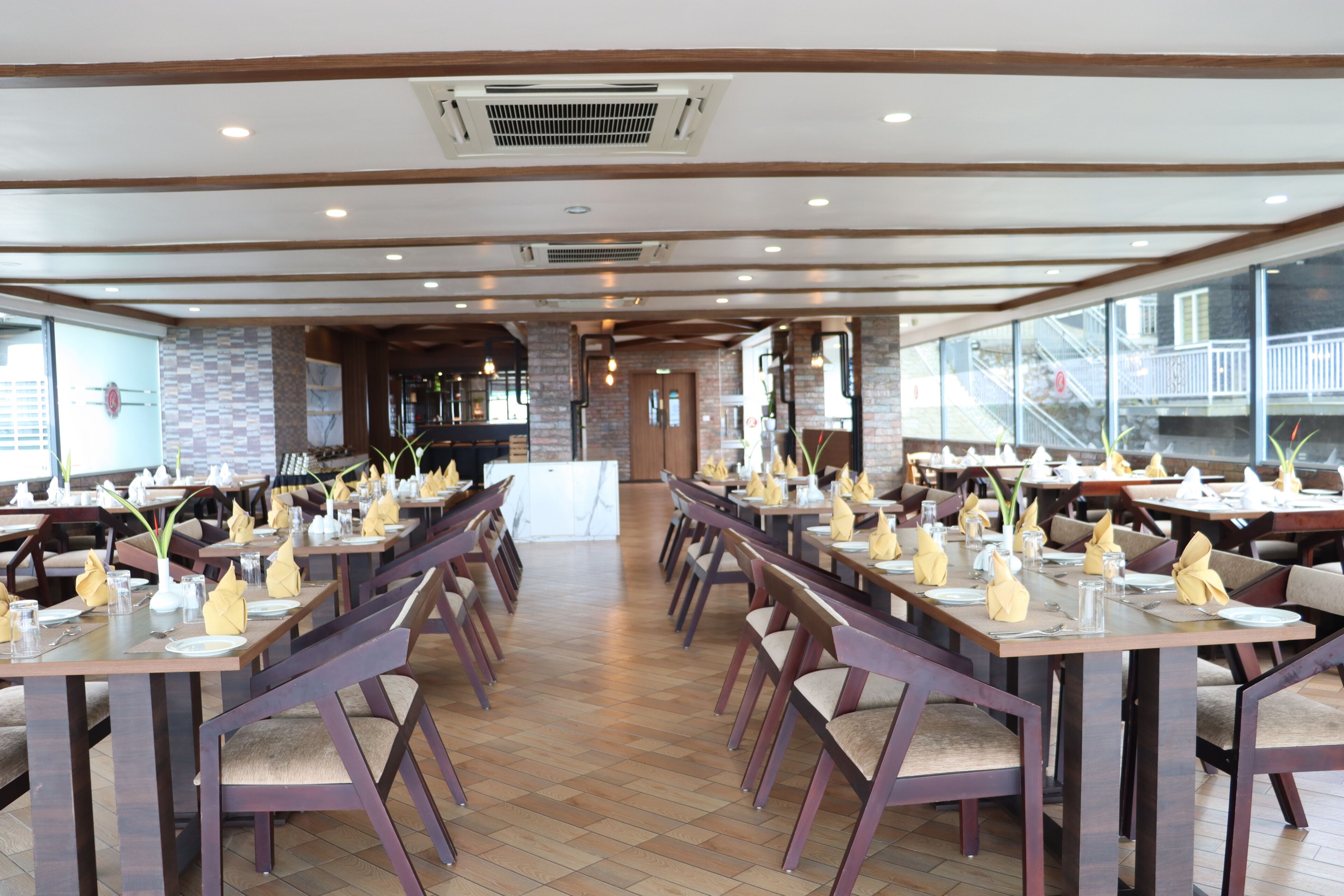 A restaurant with multiple tables set for dining, featuring a modern interior with wooden beams and a brick wall.