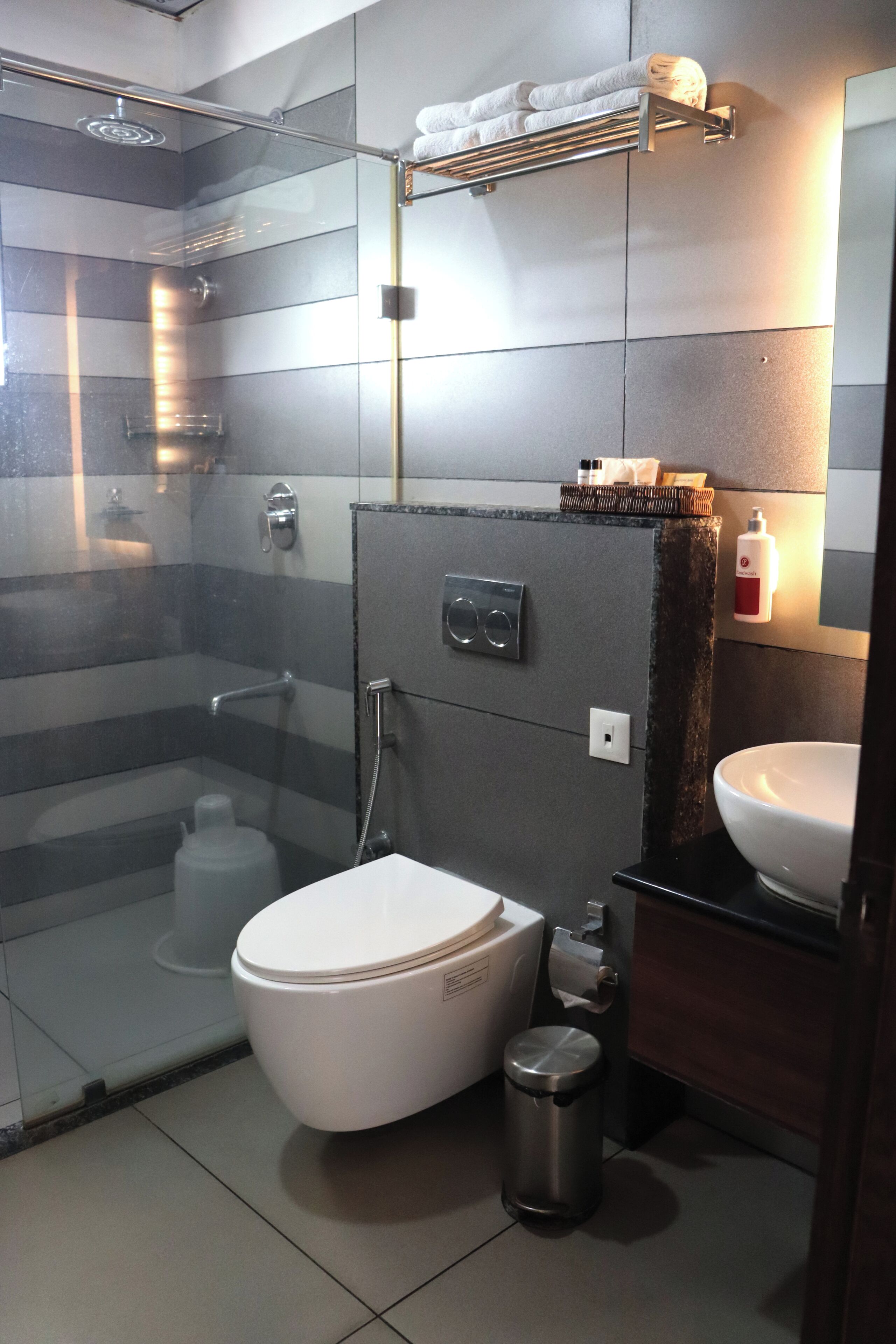 A modern bathroom with a glass shower enclosure, a white toilet, a sink, and a hand dryer.