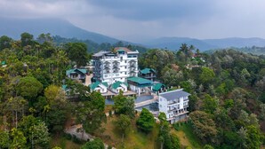 A multi-story hotel with a green roof, surrounded by dense forest and mountains in the background. - Ramee Wolkenburg Resort and Spa Munnar (Devikolam)