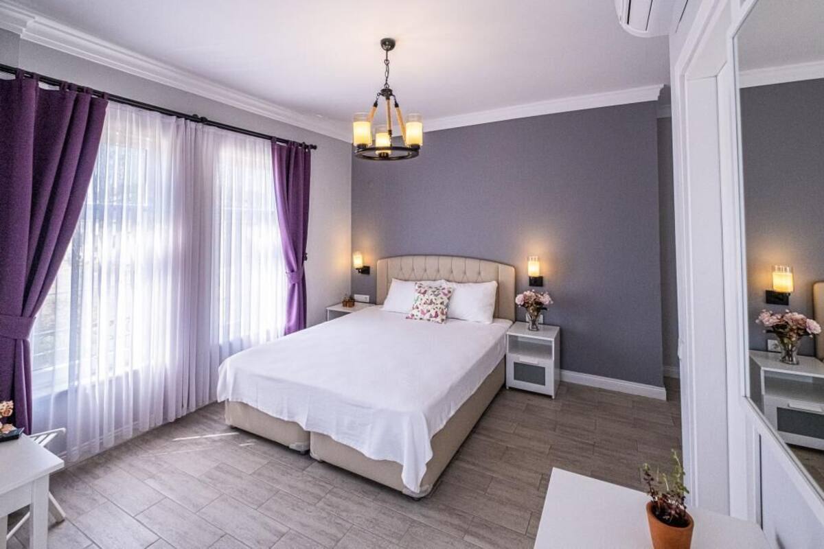 A bedroom with a large bed, two bedside tables, a chandelier, and a window with curtains.