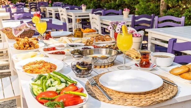 Un área de comedor al aire libre con mesas preparadas para el desayuno, incluyendo platos de comida, bebidas y aderezos.