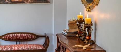 A wooden bench with a patterned cushion, a small wooden table with books and candles, and a mirror on the wall.