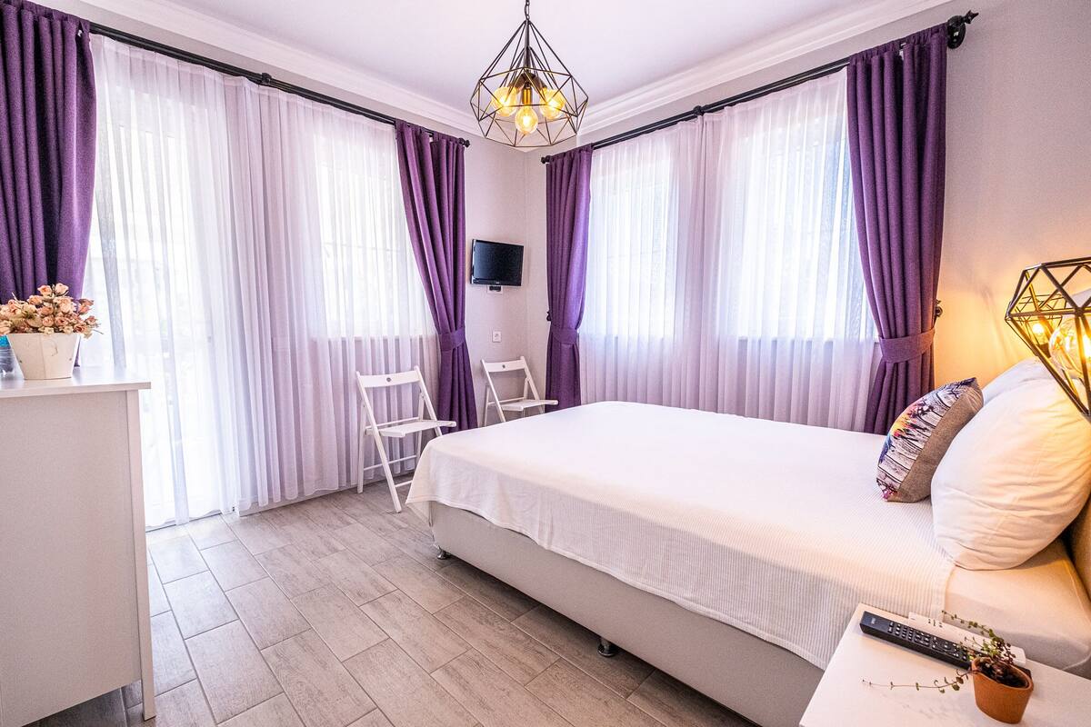 A bedroom with a bed, a desk, a chair, a TV, and a decorative light fixture.