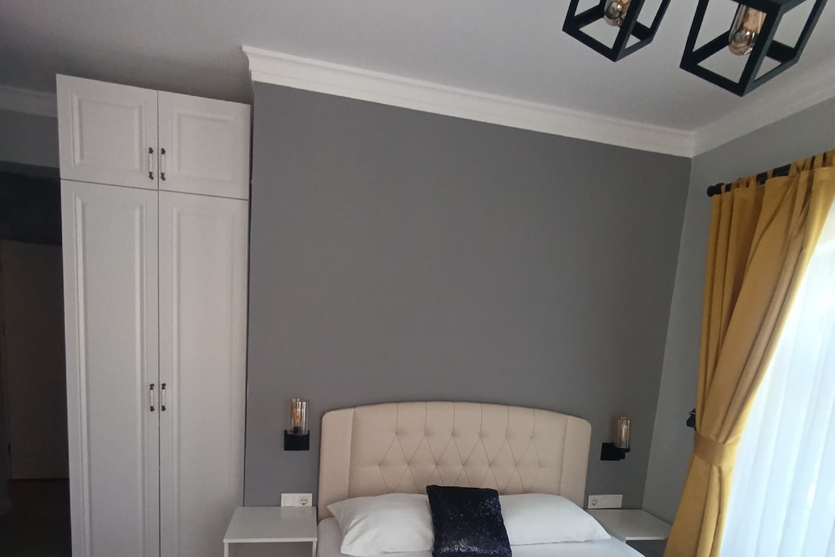 Un dormitorio con cama, mesitas de noche, un armario y una lámpara colgante.