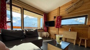 A cozy living room with a sofa, a wooden coffee table, and a TV mounted on the wall. Large windows offer a view of a snowy mountain landscape. - Magnificent apartment with stunning views❤️Schuss⛷ (Tignes)