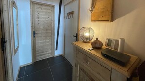 A hallway with a wooden door, a wall-mounted light fixture, a small table with a remote control, a decorative vase, and a microwave. - Magnificent apartment with stunning views❤️Schuss⛷ (Tignes)