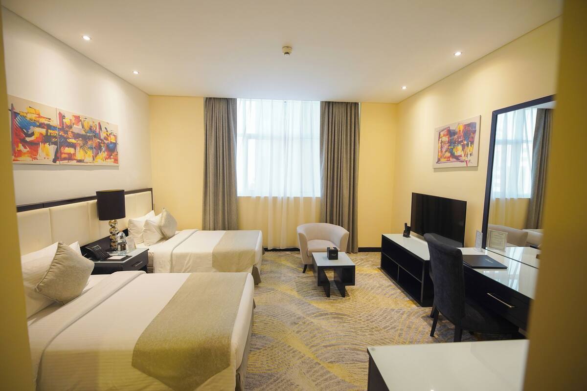 Ein Hotelzimmer mit zwei Betten, einem Schreibtisch, einem Sessel, einem Fernseher und Kunstwerken an den Wänden.