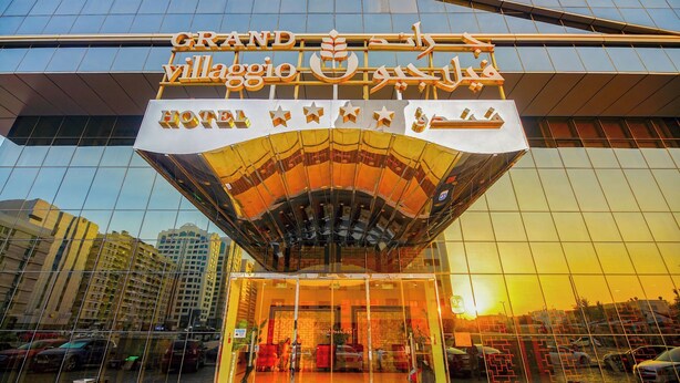 A hotel entrance with a modern glass facade and a sign in multiple languages. - Grand Villaggio Hotel Abu Dhabi (Abu Dhabi)