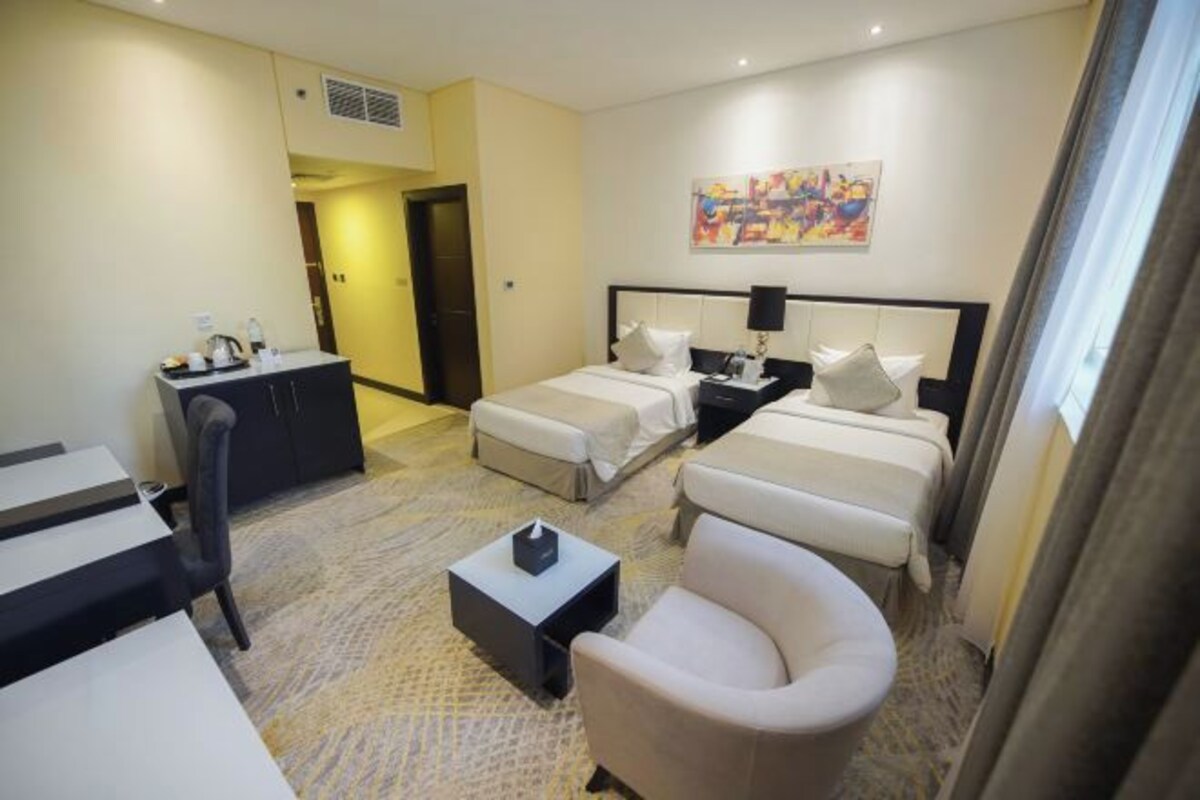 A hotel room with two beds, a desk, a chair, and a small table with a tissue box.