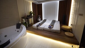 A modern bedroom with a large bathtub, a bed with two pillows, and a small round seating area. - Grand Villaggio Hotel Abu Dhabi (Abu Dhabi)