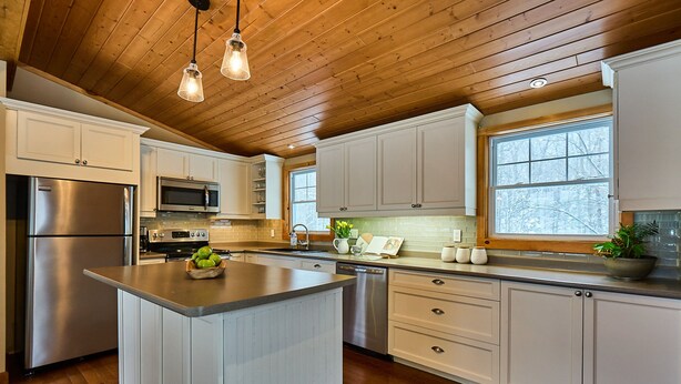 Una cocina moderna con armarios blancos, electrodomésticos de acero inoxidable y techo de madera.