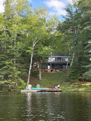 A house with a deck and a dock extending into a lake surrounded by trees.