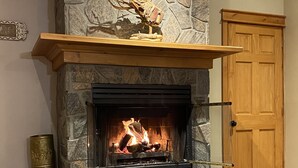 Una chimenea de piedra con repisa de madera, fuego encendido y una puerta al fondo.