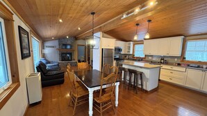 Una cocina amplia con suelo de madera, una isla central, armarios blancos y una chimenea de piedra.