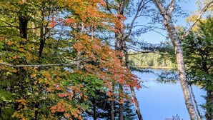 Una cabaña junto al lago con sillas Adirondack y un muelle que se adentra en el agua.