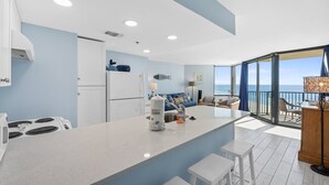 Una cocina moderna con una isla central, un comedor con vistas al océano y un balcón con barandilla y sillas.