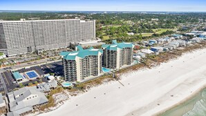 Un hotel frente a la playa con varios edificios altos, un estacionamiento y una playa.
