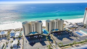 A beachfront hotel with two prominent buildings, a parking lot, and a view of the ocean. - Beachfront Paradise Condo ON THE BEACH/FREE BEACH CHAIRS/5 STARS & BEACH VIEWS (Panama City Beach)