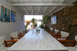 A long wooden table with white chairs, a stone wall, and artwork on the walls.