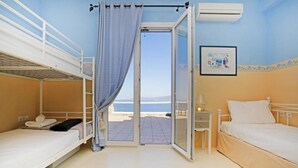 A room with two beds, a window with a curtain, a bedside table with a lamp, and a picture on the wall. - Amati Villa Cavo Dellos (Mykonos)