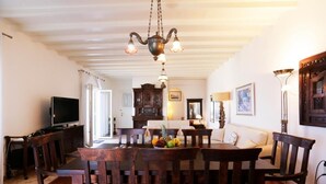 A dining area with a wooden table and chairs, a chandelier, and a television in the background. - Amati Villa Cavo Dellos (Mykonos)