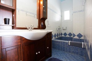 A bathroom with a wooden vanity, a white sink, a bathtub, and blue patterned tiles.