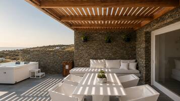 Terraza en la azotea con muro de piedra, pérgola de madera, mobiliario exterior blanco y un jacuzzi.