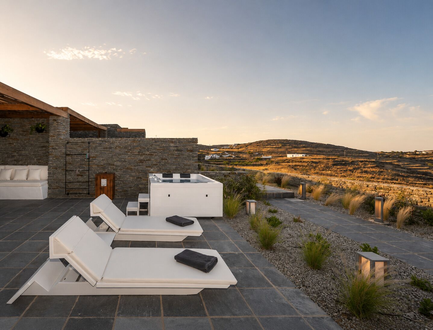 Een terras op het dak met loungestoelen, een stenen muur en uitzicht op een glooiend landschap.