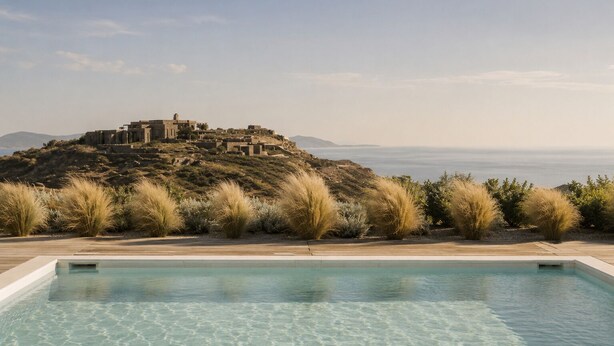Ein Pool mit klarem Wasser, eine Holzterrasse und Blick auf einen Hügel mit Gebäuden.
