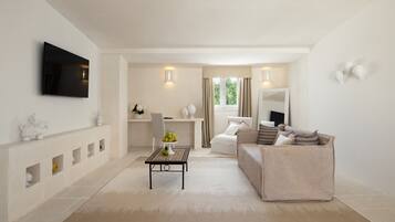 A modern living room with a flat-screen TV, a sofa, a coffee table with a fruit bowl, and a dining area with a chair and a small table.
