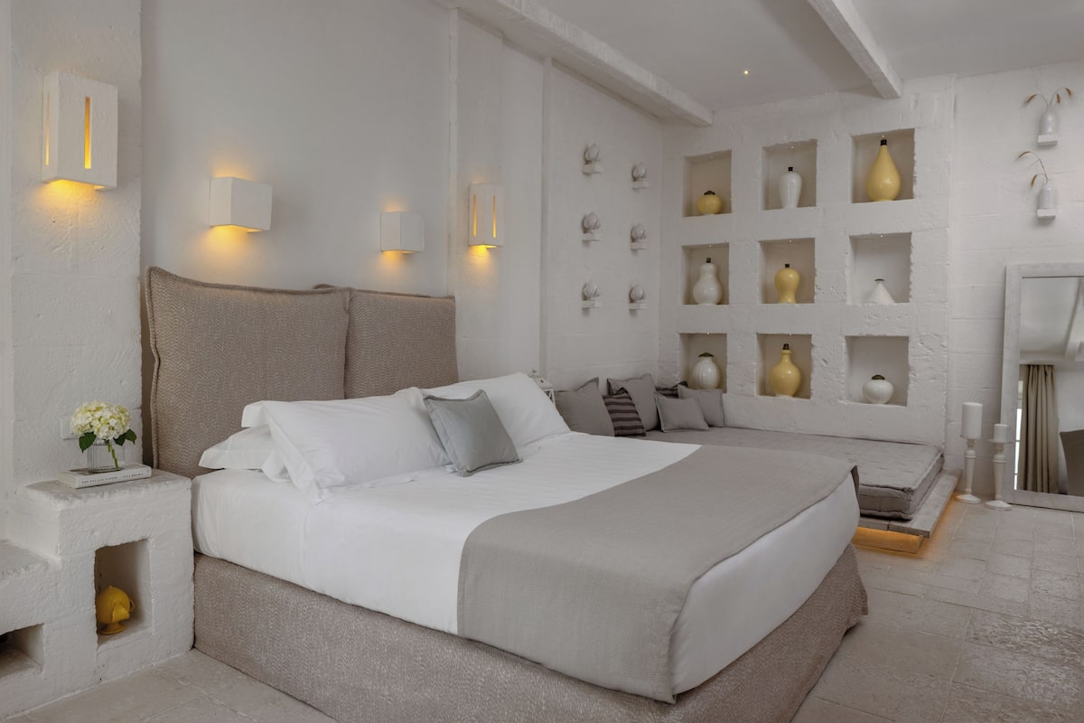 Un dormitorio con una cama grande, mesitas de noche, un estante en la pared con adornos y un espejo.