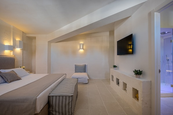 Une chambre à coucher moderne avec un grand lit, un plus petit lit, un banc, une télévision et une cheminée.