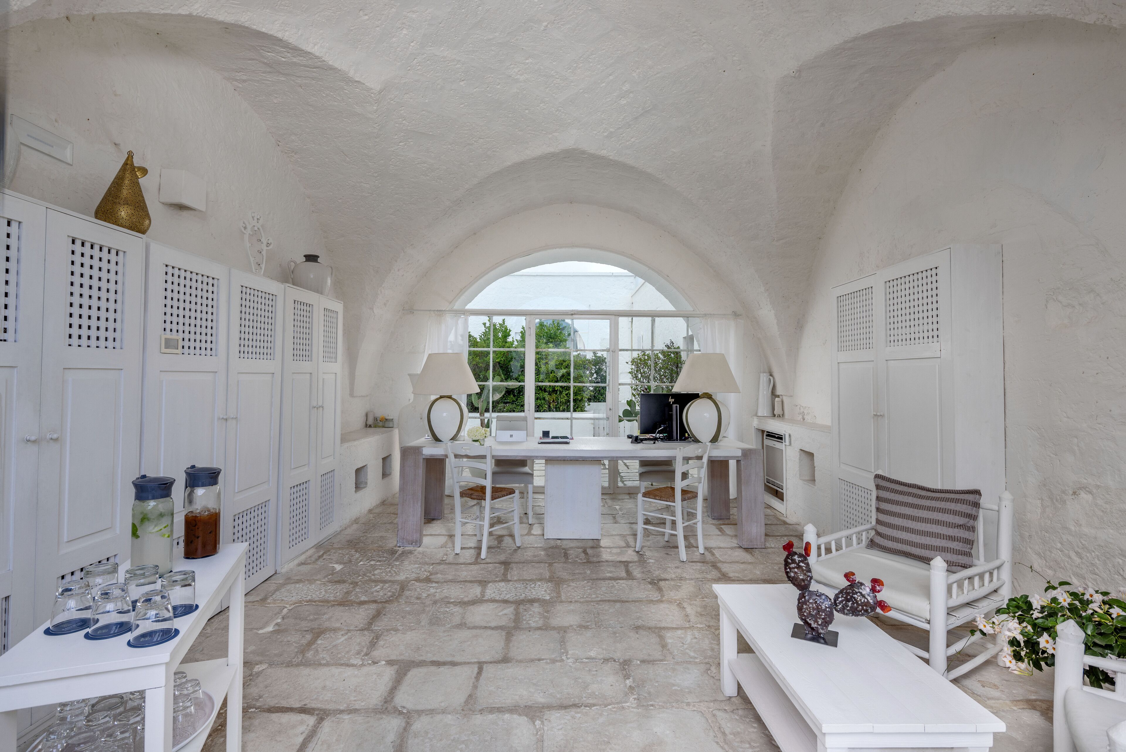 A white interior with a stone floor, white furniture, and a large arched window.
