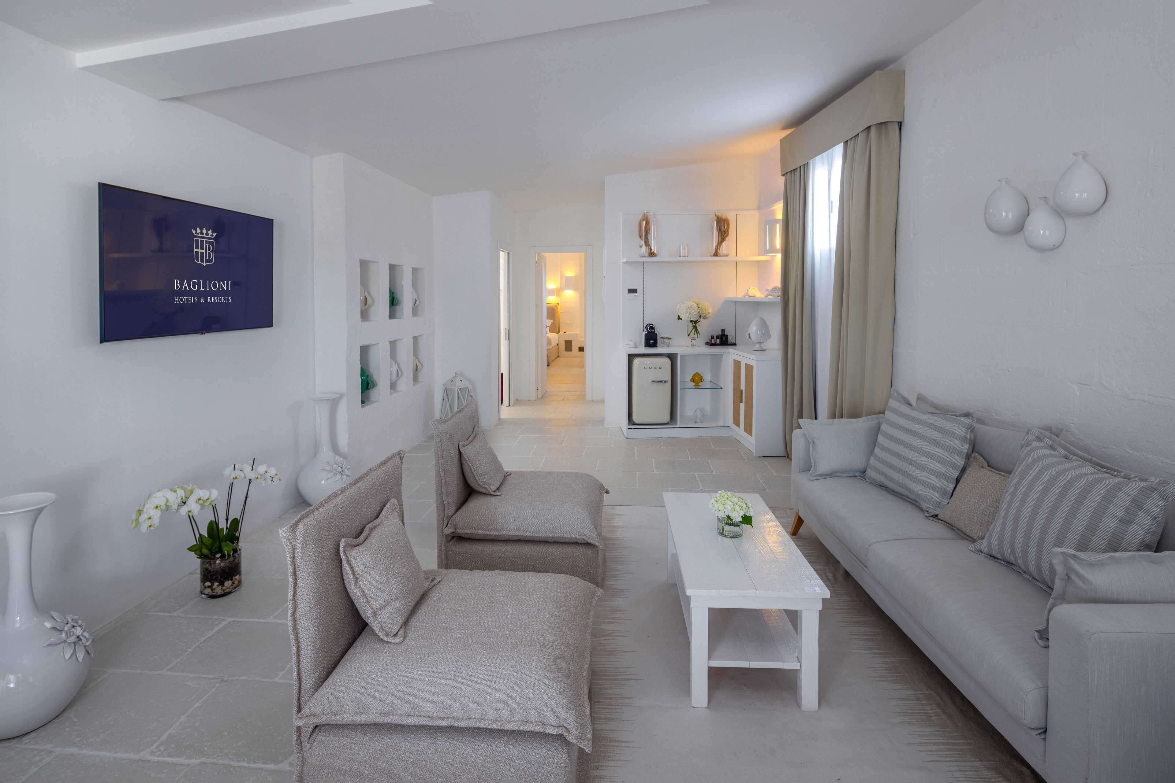A modern living room with a sofa, a coffee table, and decorative vases. There is a television mounted on the wall displaying a logo.