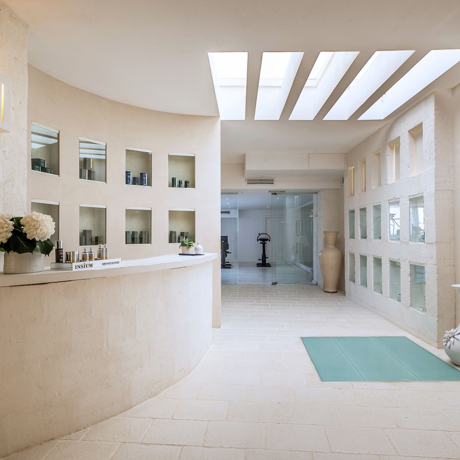 A spacious corridor with a skylight, a reception desk with a vase of flowers, and a yoga mat on the floor.