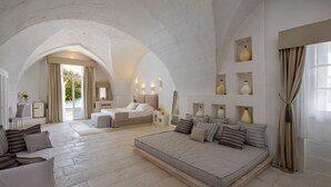 Une chambre spacieuse avec un grand lit, un canapé et un coin bureau. On y trouve plusieurs lampes et une grande fenêtre avec des rideaux.