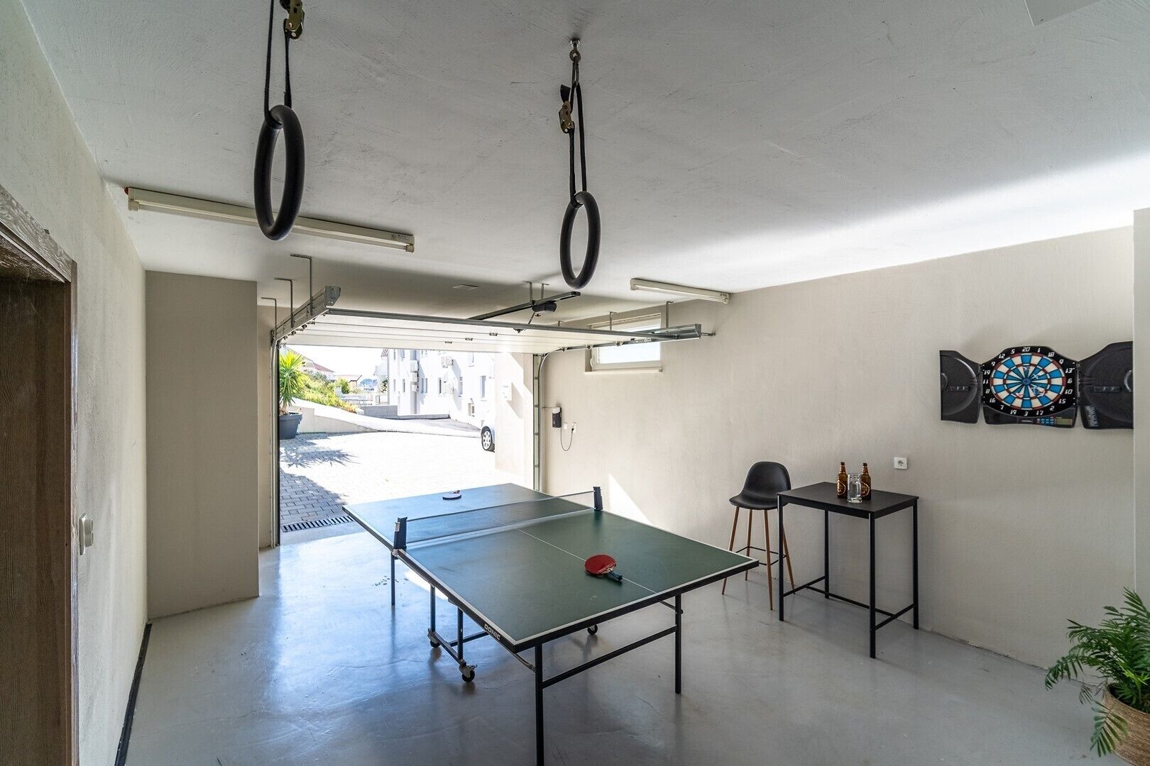 Une pièce avec une table de ping-pong, un jeu de fléchettes et une petite table sur laquelle sont posées des bouteilles.