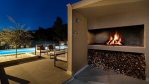 Une terrasse extérieure avec une piscine, des chaises longues et une cheminée à bois.