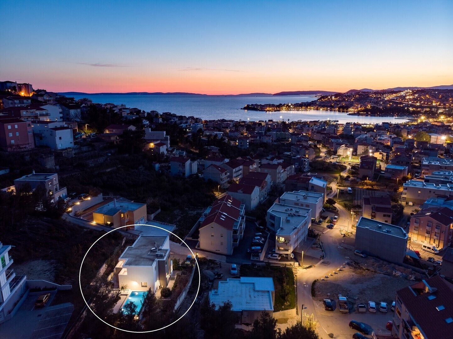 Un pueblo costero al atardecer con vistas al mar y una zona destacada que muestra un edificio moderno con piscina.