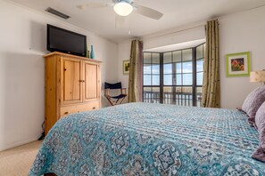 A bedroom with a bed, a wooden wardrobe, a television on top, a window with curtains, and a balcony. - Blue Bayou - 1912 Cadillac 4 Bedroom Home by RedAwning (Dauphin Island)