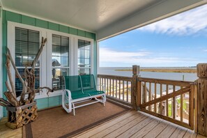 A covered porch with a green bench, wooden railings, and a view of a body of water. - Blue Bayou - 1912 Cadillac 4 Bedroom Home by RedAwning (Dauphin Island)