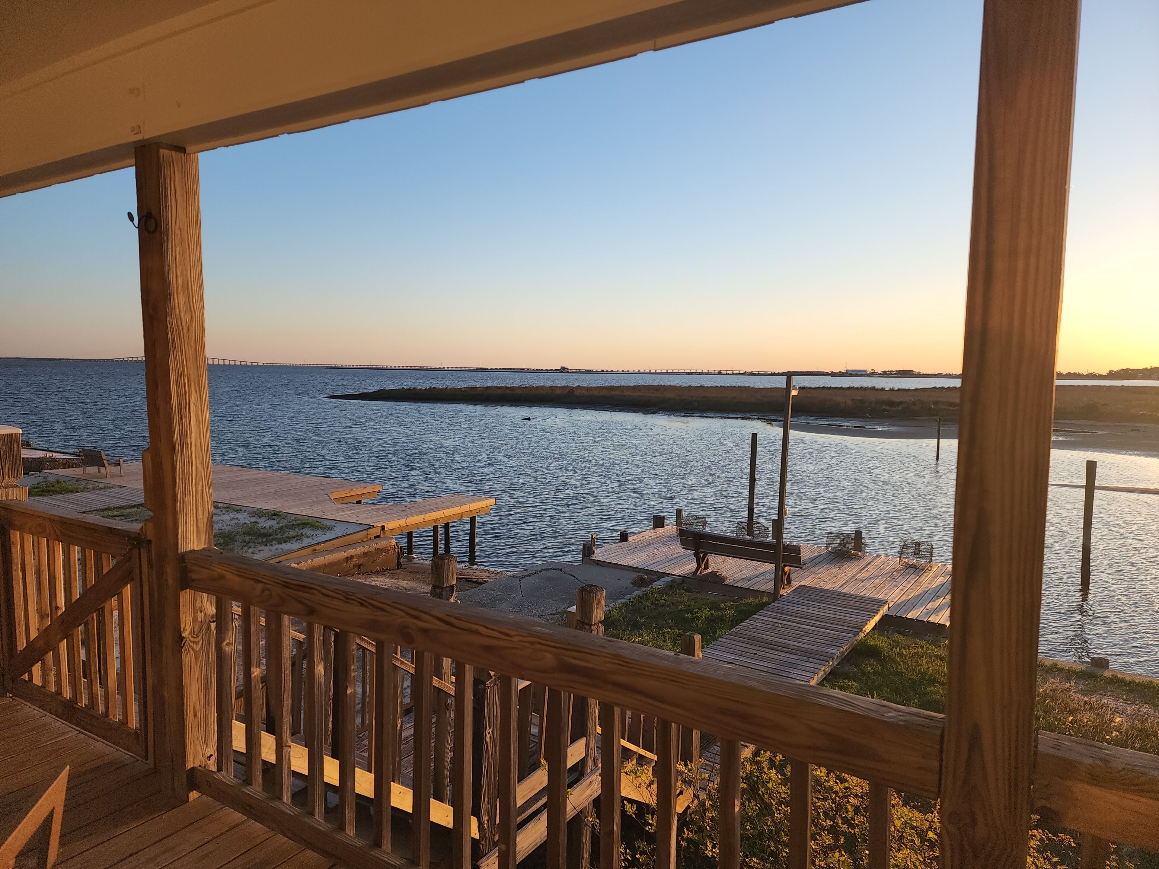 A wooden deck with a view of a calm body of water and a distant bridge.