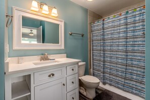A bathroom with a white vanity, a mirror with lights, a toilet, and a shower curtain. - Blue Bayou - 1912 Cadillac 4 Bedroom Home by RedAwning (Dauphin Island)
